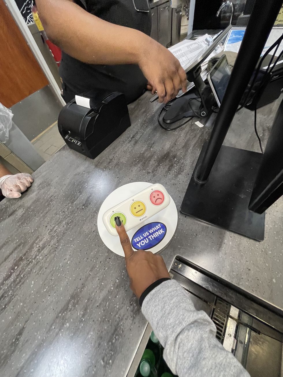 Person pressing green smiley button on a feedback device at a counter.