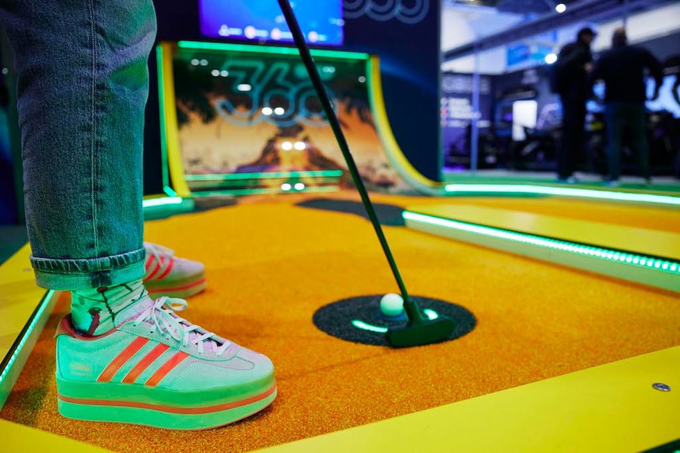 Person putting golf ball on neon-lit mini-golf course with colorful sneakers.