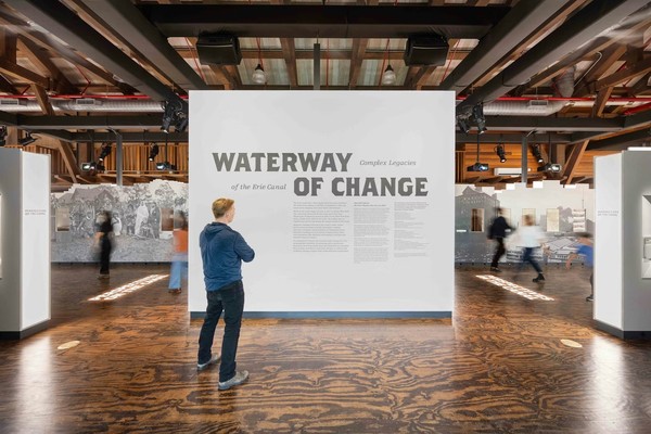 Person reading "Waterway of Change" exhibit text on a large display in a museum.