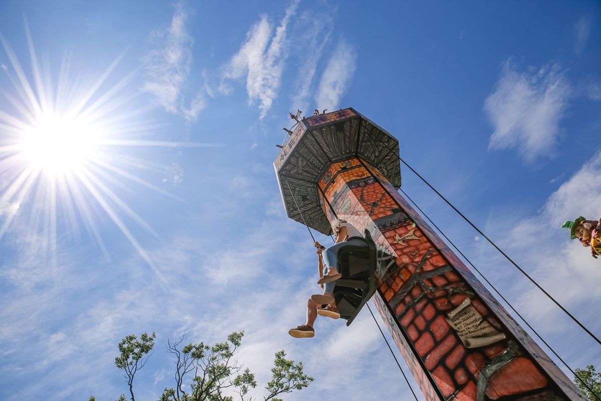 Person rides a drop tower against a bright sun and blue sky.