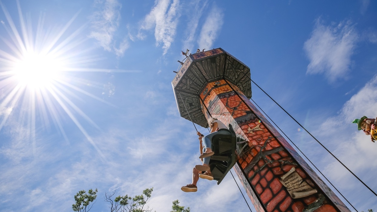 Person rides a drop tower against a bright sun and blue sky.
