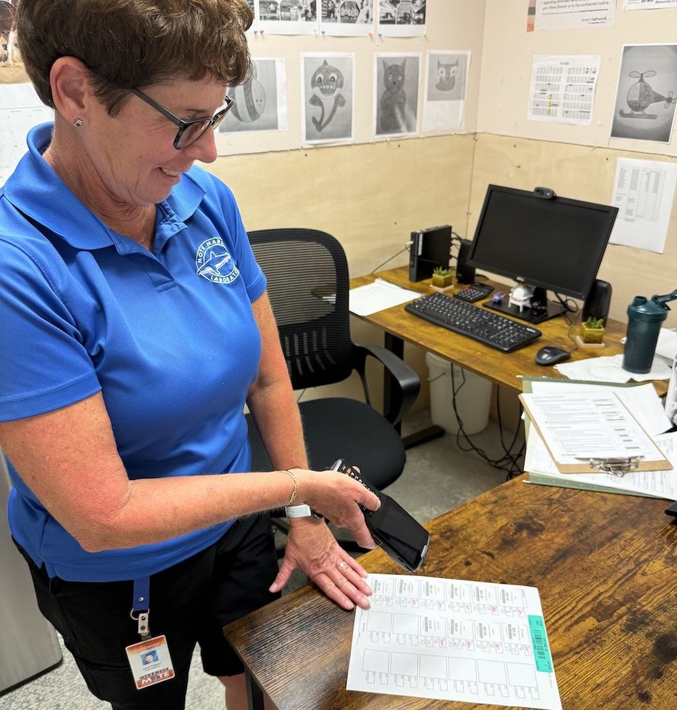Person scanning inventory management document with phone in an office, wearing a blue polo and glasses.