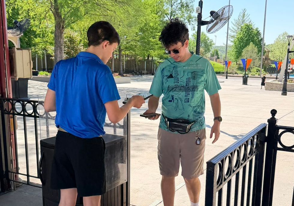 Person scanning ticket at a gate at six flags st louis on a sunny day, surrounded by greenery.