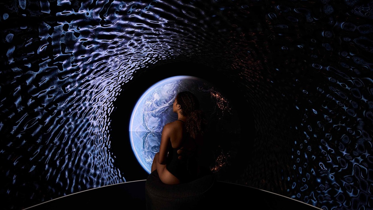 Person seated in a dark room, gazing at a projection of Earth with textured walls.
