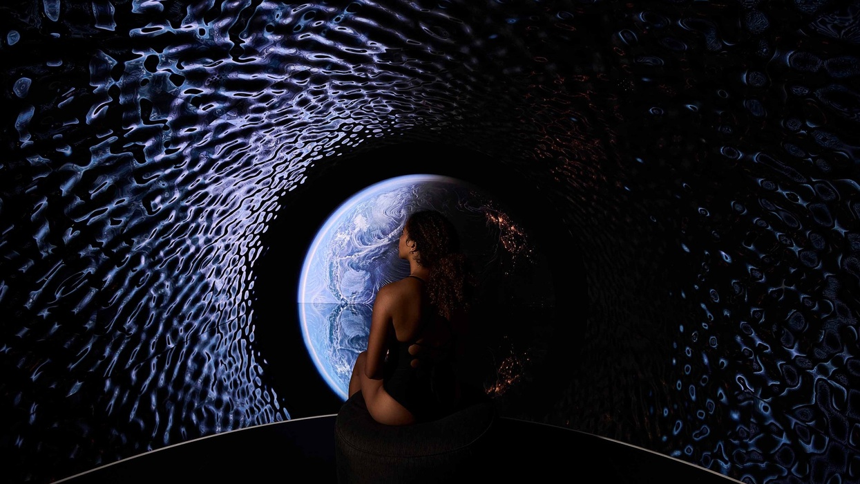 Person seated in a dark room, gazing at a projection of Earth with textured walls.