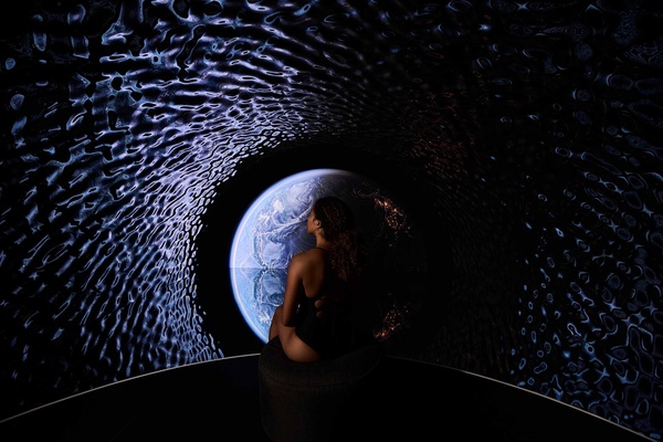 Person seated in a dark room, gazing at a projection of Earth with textured walls.