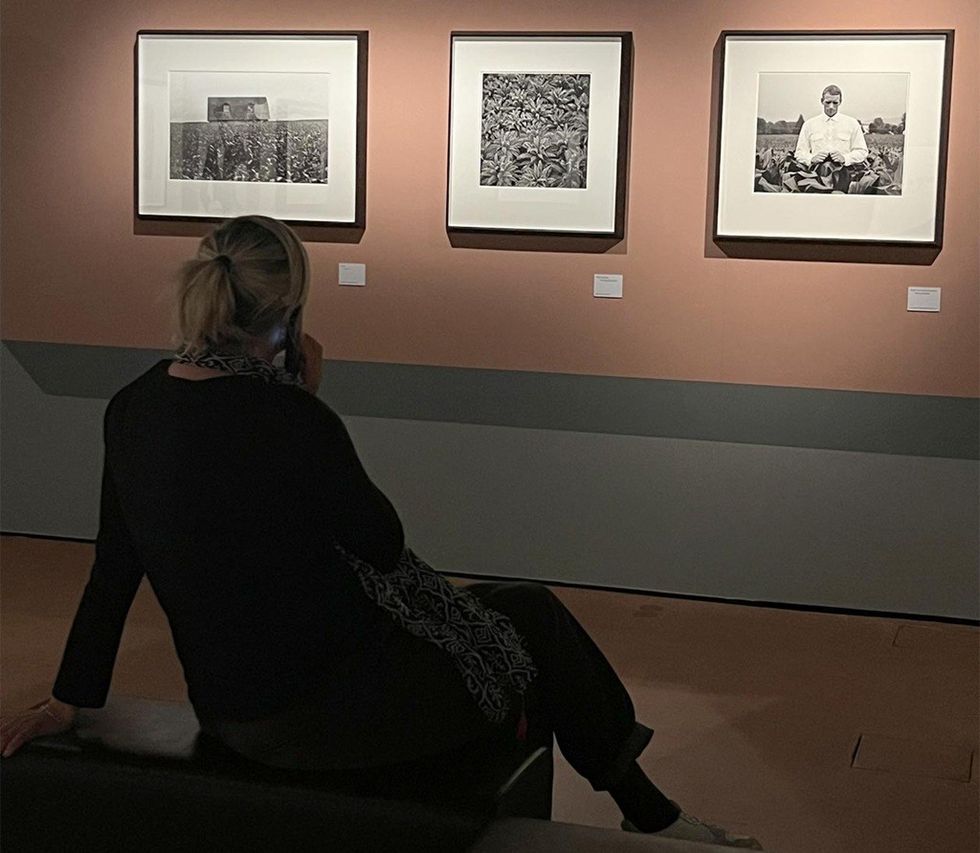 Person seated, viewing black-and-white framed photos in a dimly lit gallery.