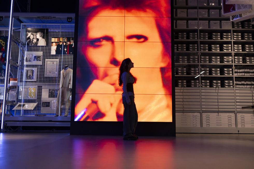 Person silhouetted against a large portrait of David Bowie and archival exhibition.