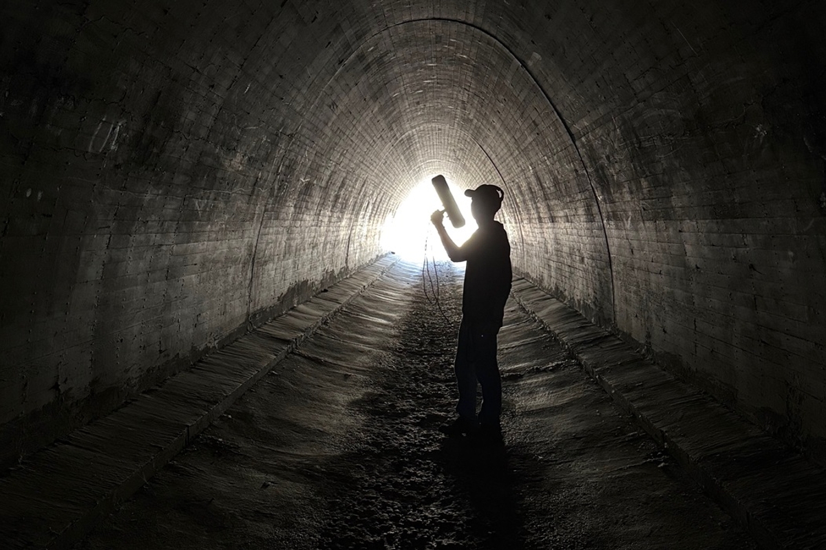 Person silhouetted in tunnel with light at the end, holding a cylindrical object.