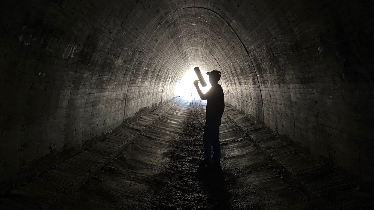 Person silhouetted in tunnel with light at the end, holding a cylindrical object.