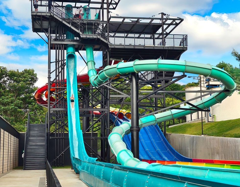Person sliding down a tall, winding waterslide at a water park under a blue sky.