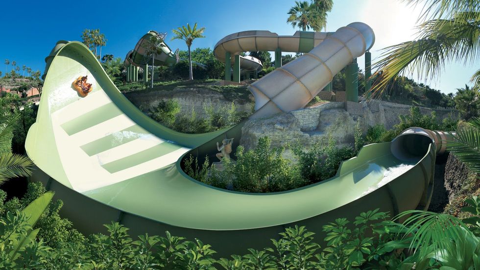 Person sliding on a large green water slide with lush vegetation around at Siam Park
