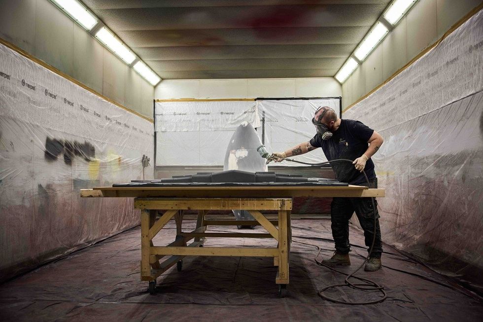 Person spray painting in a workshop spray booth, wearing a mask and protective gear.