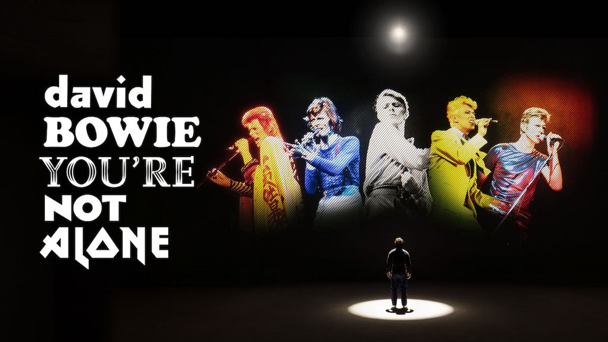 Person standing, admiring colorful concert images with "David Bowie You're Not Alone" text.