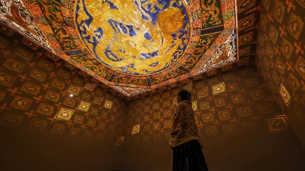 Person stands in ornate room with a dragon mural on ceiling.