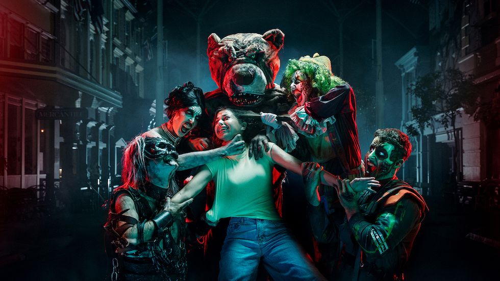 Person surrounded by costumed creatures in a spooky, dimly-lit street setting.