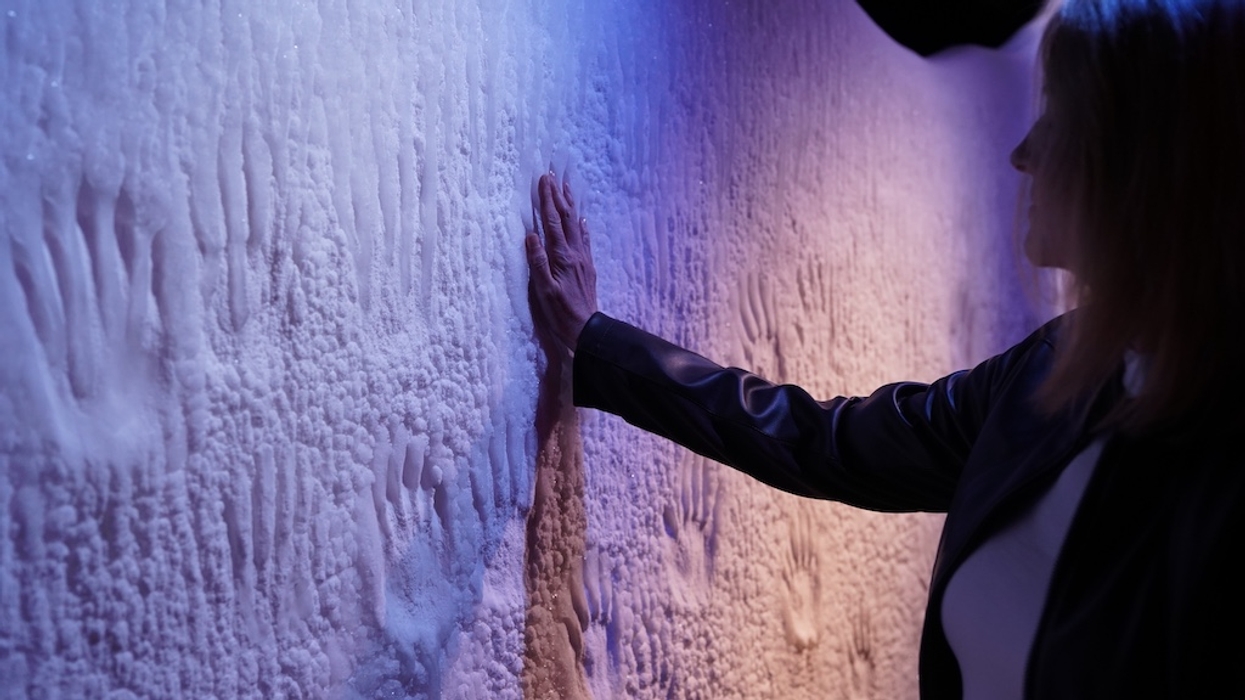 Person touching a textured, illuminated wall with handprints.