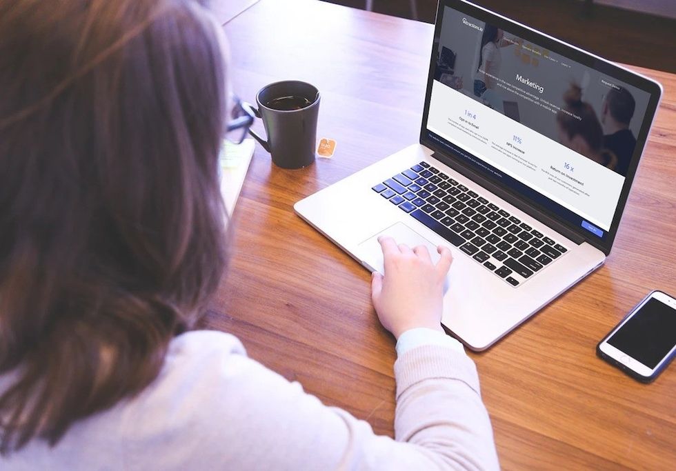 Person using a laptop with an Attractions.io marketing webpage open, next to a smartphone and a cup.