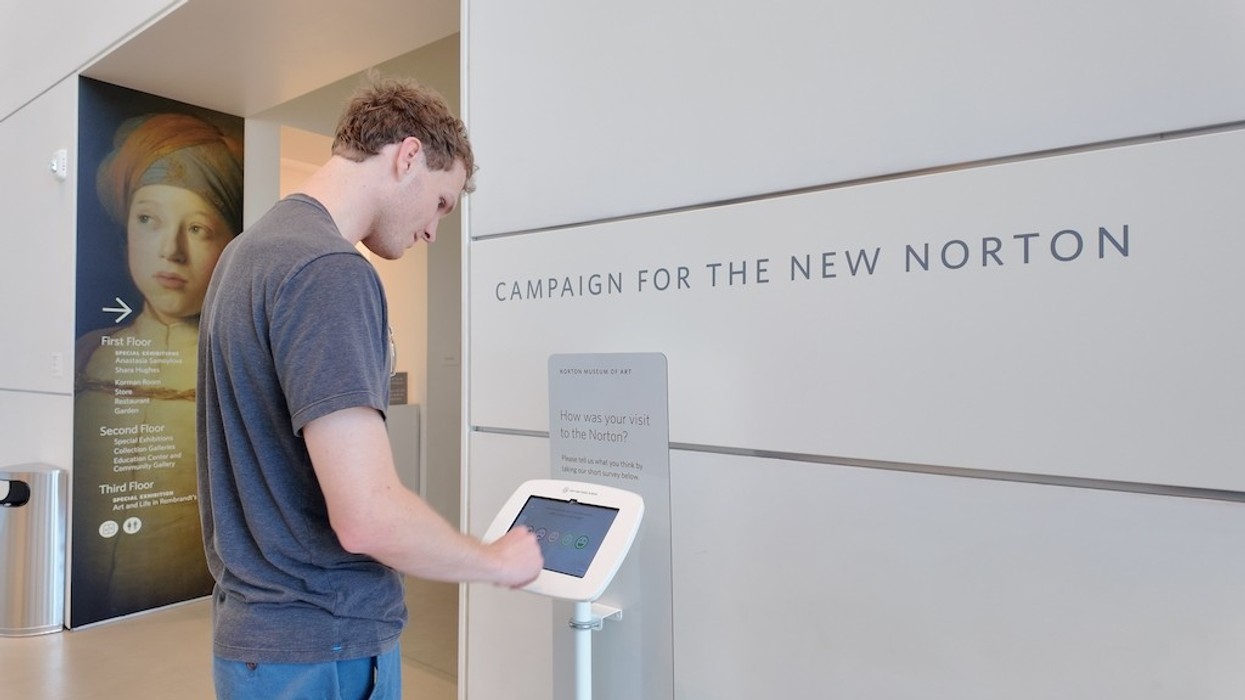 Person using a touchscreen kiosk in the Norton Museum of Art in a lobby.