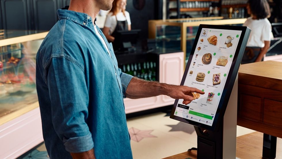 Person using a touchscreen kiosk to order pastries in a caf\u00e9.