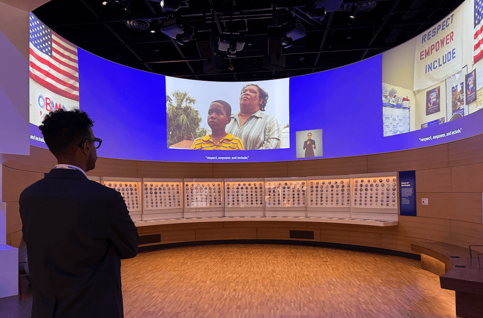 Person viewing a video in a modern museum exhibit with coin displays and inspirational text.