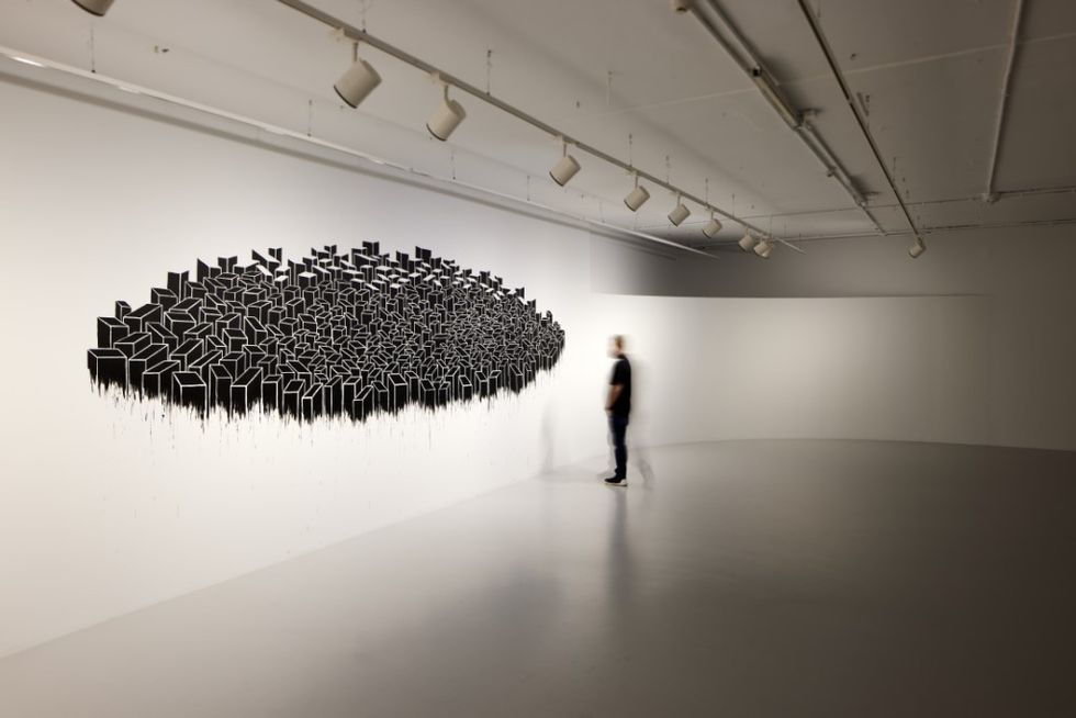 Person viewing abstract geometric wall art in a spacious, minimalist gallery at Mathaf: Arab Museum of Modern Art
