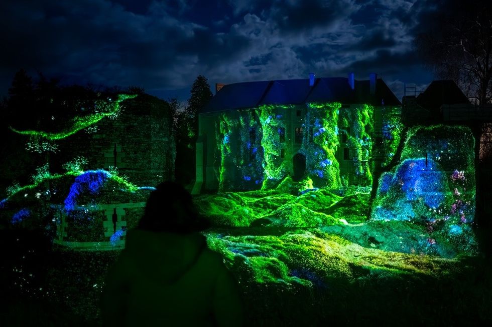 Person viewing colorful, luminous projections on a historic building at night.
