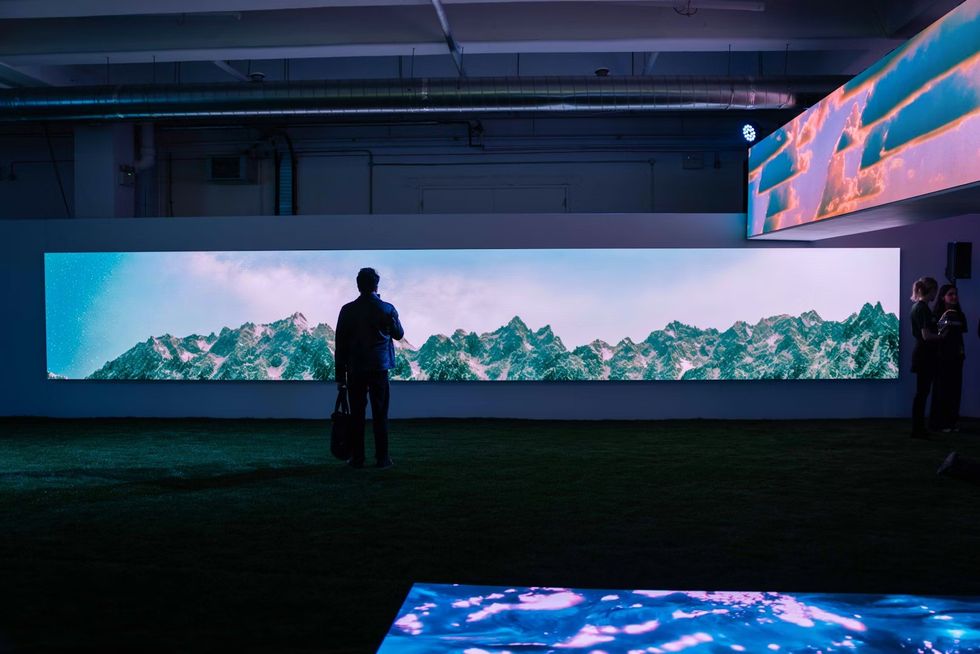 Person viewing mountain landscape on a large digital screen in a dimly lit room at SXSW London