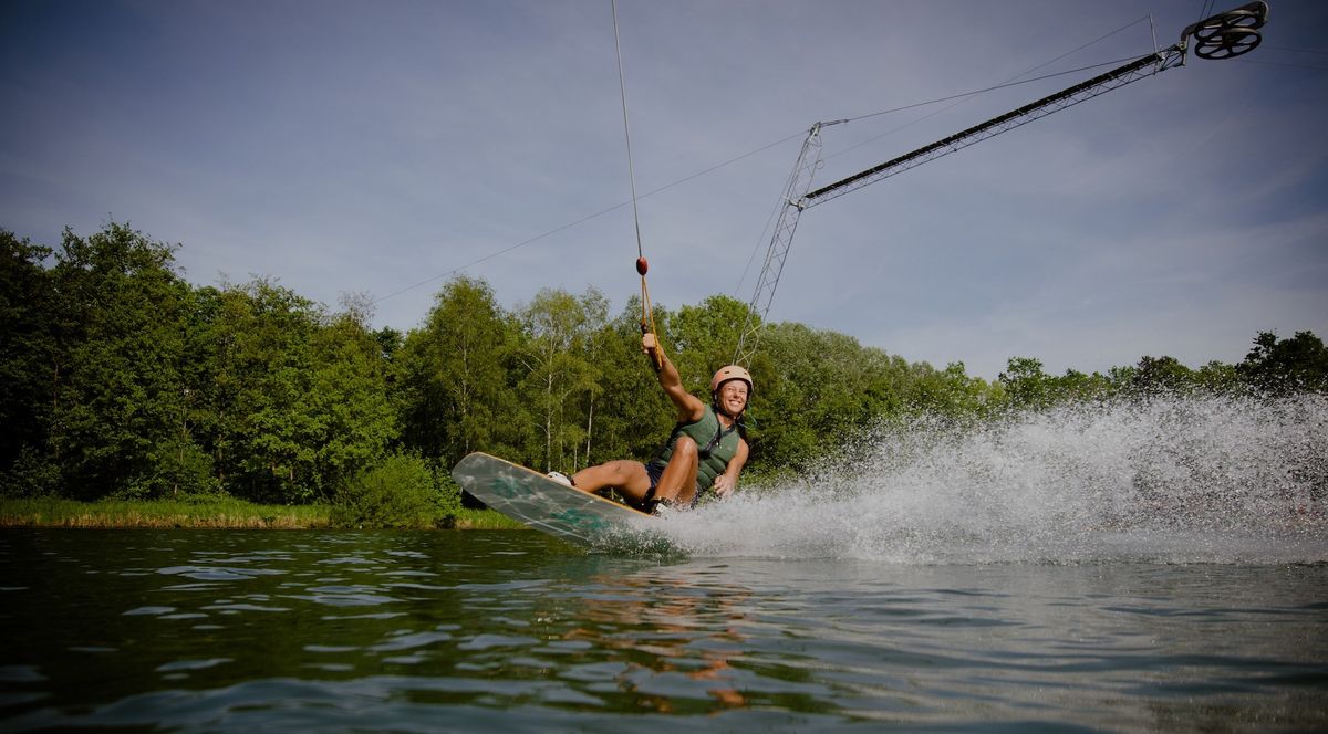 Person wakeboarding on a lake with trees and clear sky in the background.