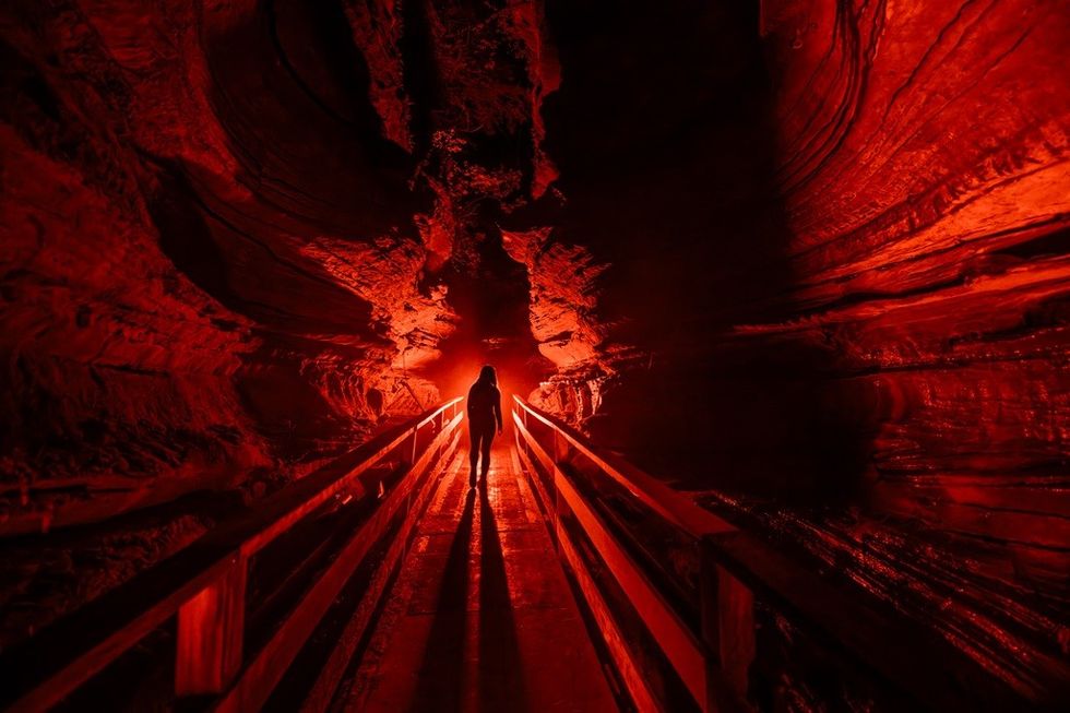 Person walks through a red-lit tunnel with rock walls.