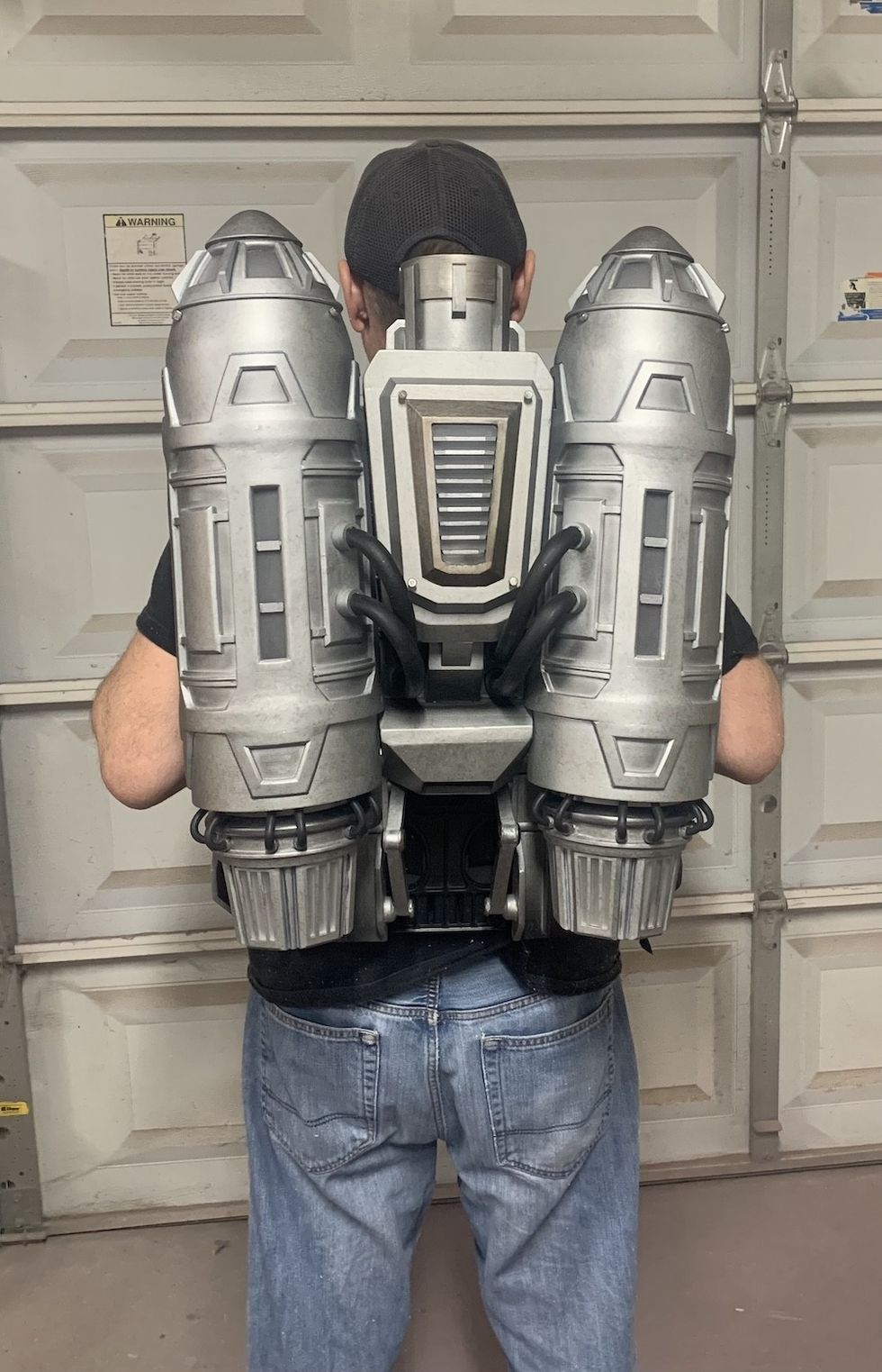 Person wearing a large, silver sci-fi jetpack in a garage.