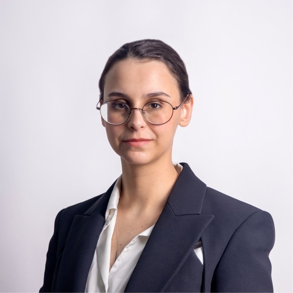 Person wearing glasses and a suit jacket with a white shirt; plain background.