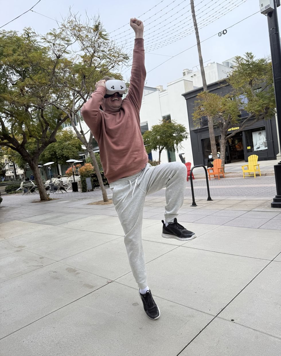 Person wearing VR headset, playfully posing outdoors with one arm raised and one leg lifted.