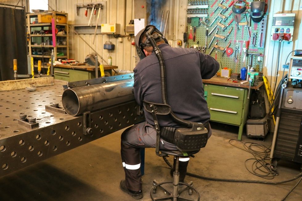Person welding metal pipe in Sunkid Heege's industrial workshop.