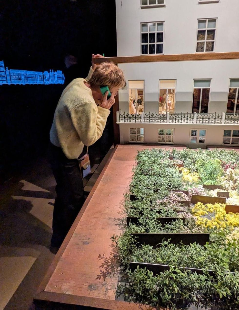 Person with audio guide examines large building model in a dimly lit room.