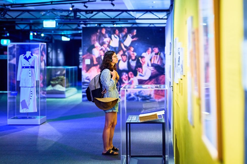 Person with backpack observes exhibits in a brightly lit museum gallery.