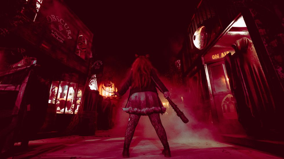 Person with bat in eerie, foggy street; red lighting enhances the spooky atmosphere.