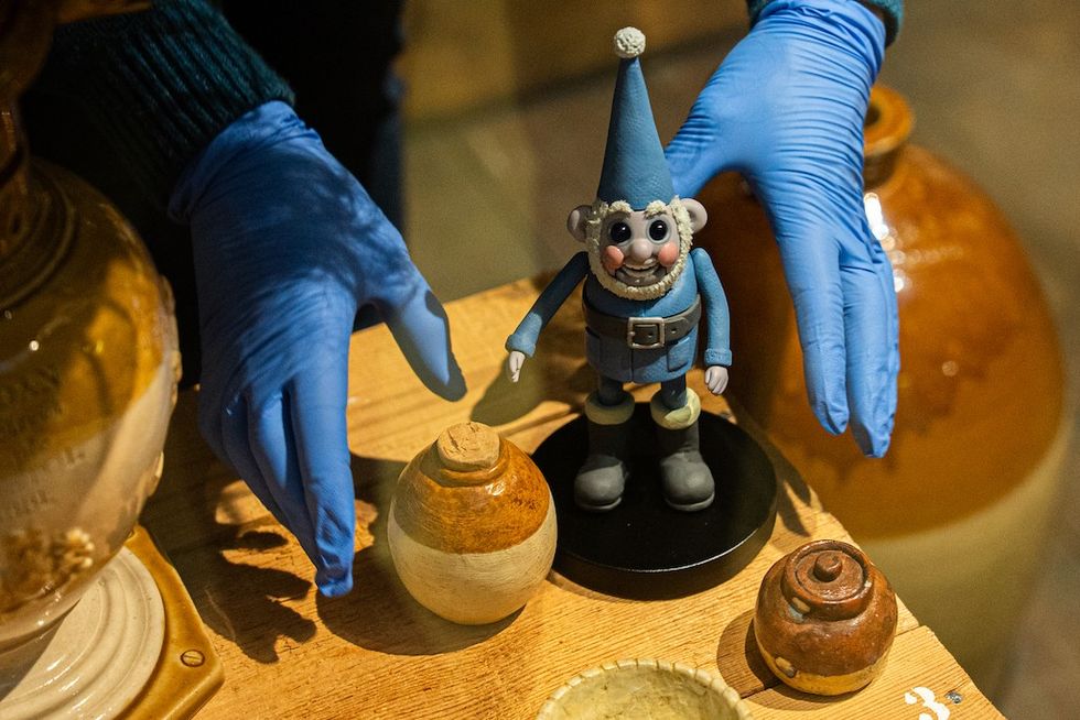 Person with blue gloves handling a Wallace and Gromit gnome figurine on a wooden table.