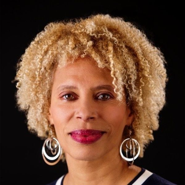 Person with curly hair and hoop earrings against a black background.