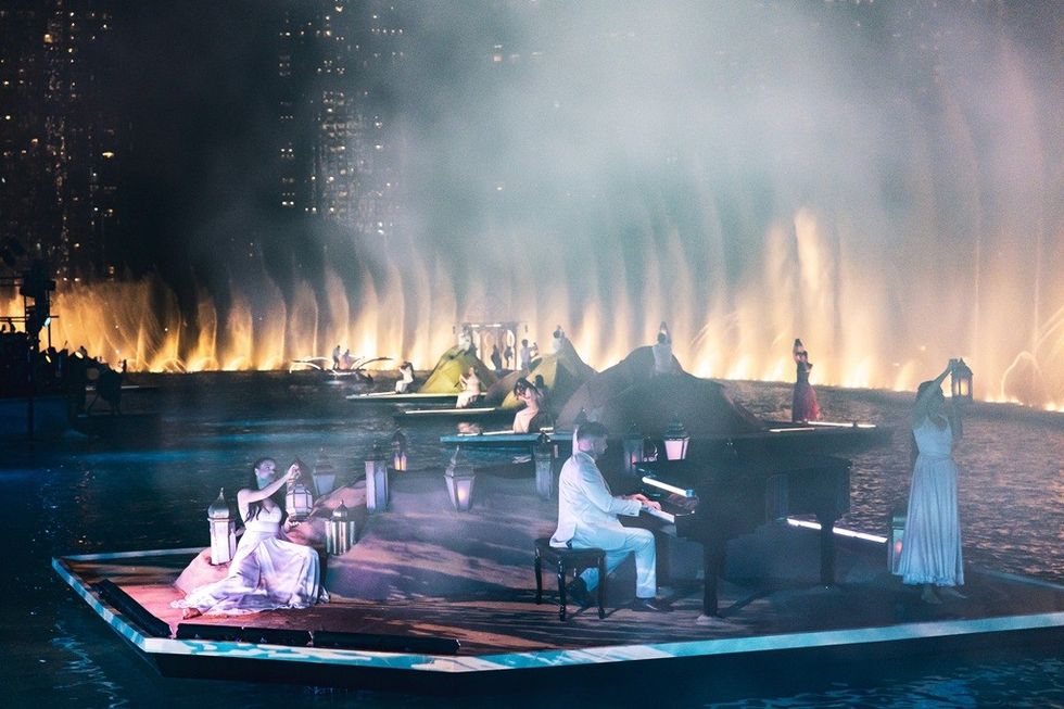 Pianist and performers on a floating stage with illuminated fountains in the background.