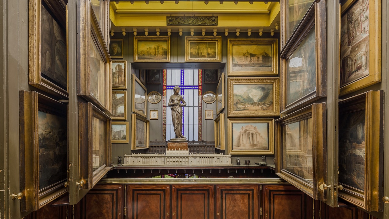 Picture Room Recess at Sir John Soane Museum. Art-filled room with framed paintings, statue, and diorama under a stained glass window.