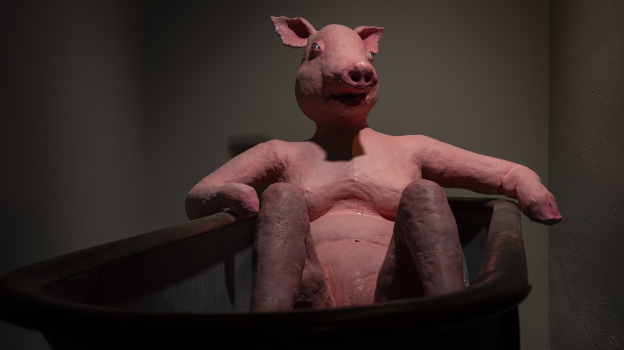 Pig sculpture called 'The Pig Lady' lounging in a bathtub under dim lighting at the Ministry of Awe.