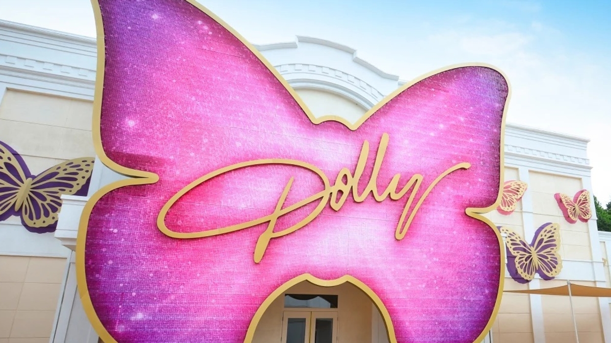 Pink butterfly sign with "Dolly" in gold script, background of a building with butterfly decor at Dollywood
