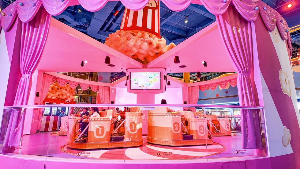 Pink popcorn-themed amusement ride with numbered seats and pink curtains.