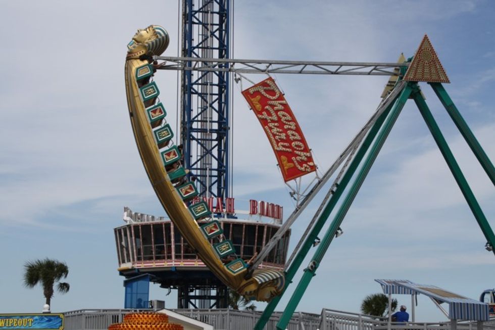Pirate ship ride swinging at an amusement park with blue sky background.