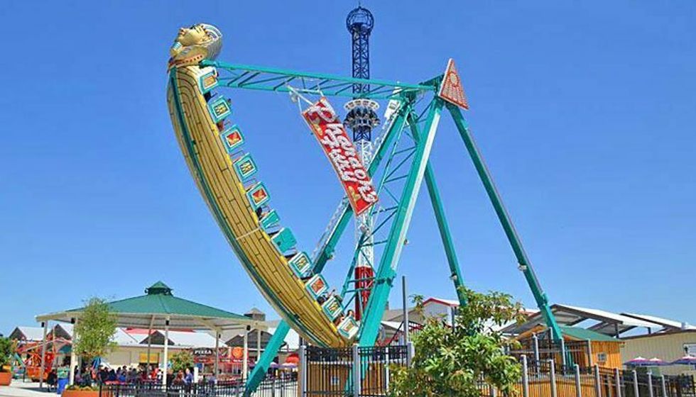 Pirate ship swing ride at an amusement park, against a clear blue sky.