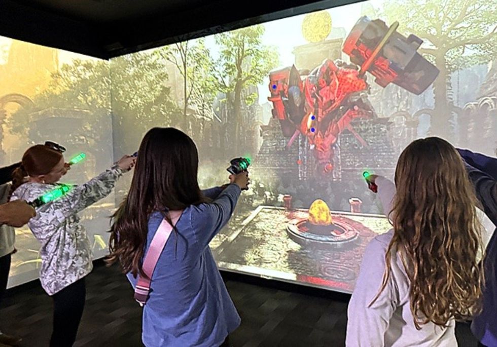 Players aim green laser guns at a virtual dragon on a large screen.