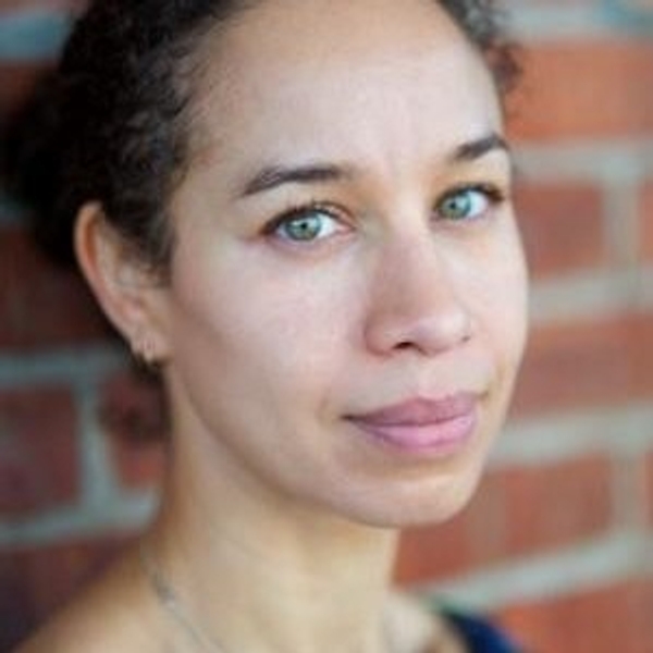 Portrait of a woman with light eyes, framed by a brick wall background.