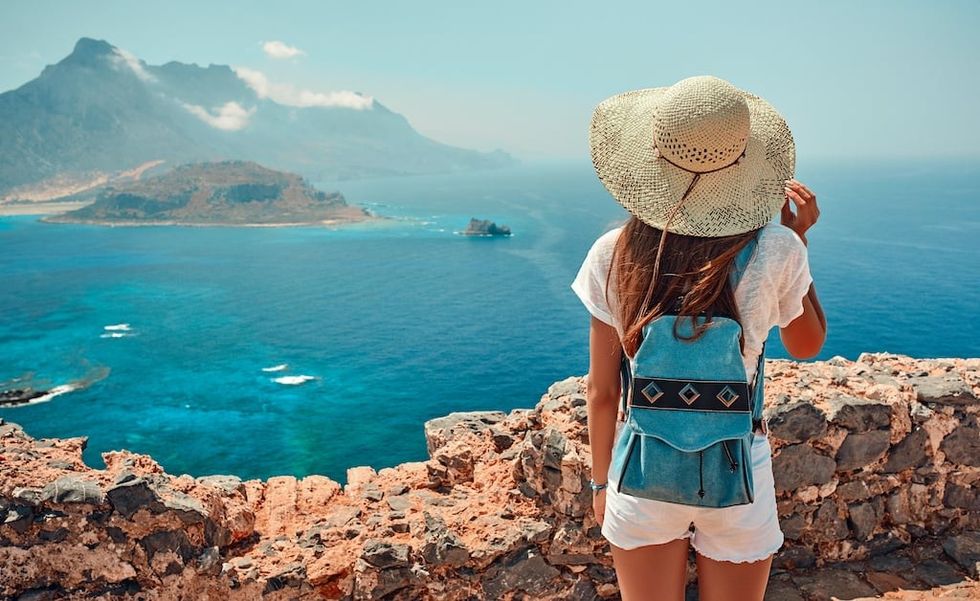 Portrait of happy girl in a hat with a backpack standing on background of mountains and sea.