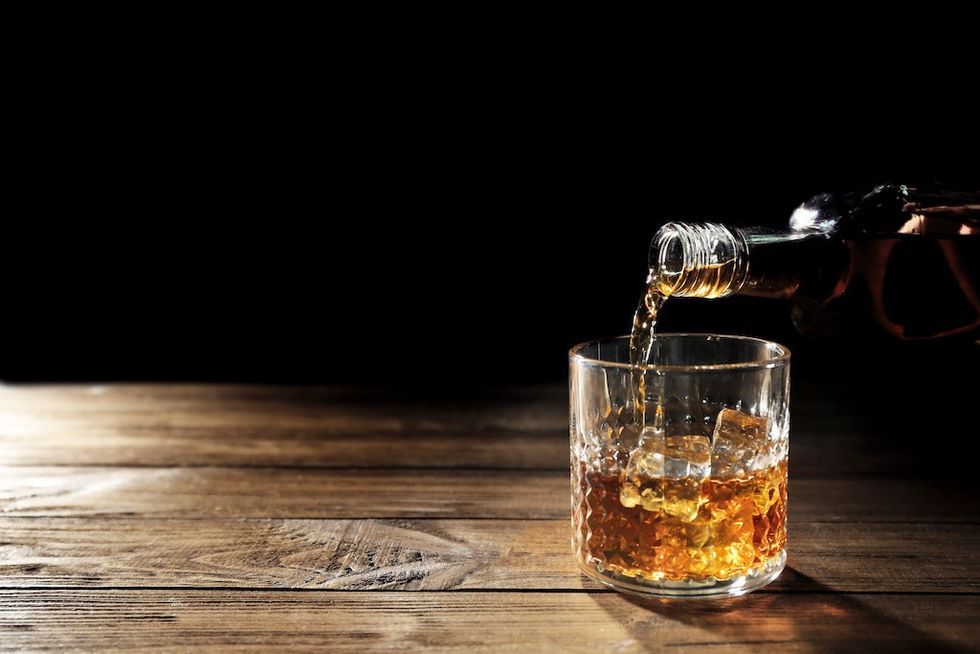 Pouring whisky into glass on wooden table closeup